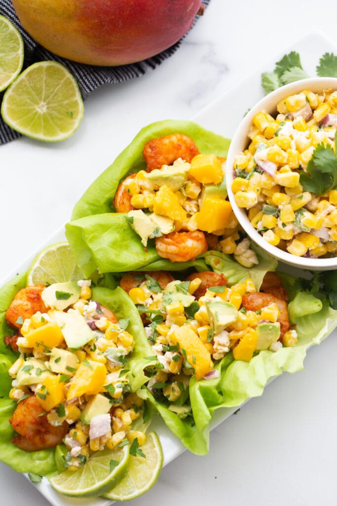 A white platter of air fryer shrimp tacos wrapped in lettuce with corn salsa 