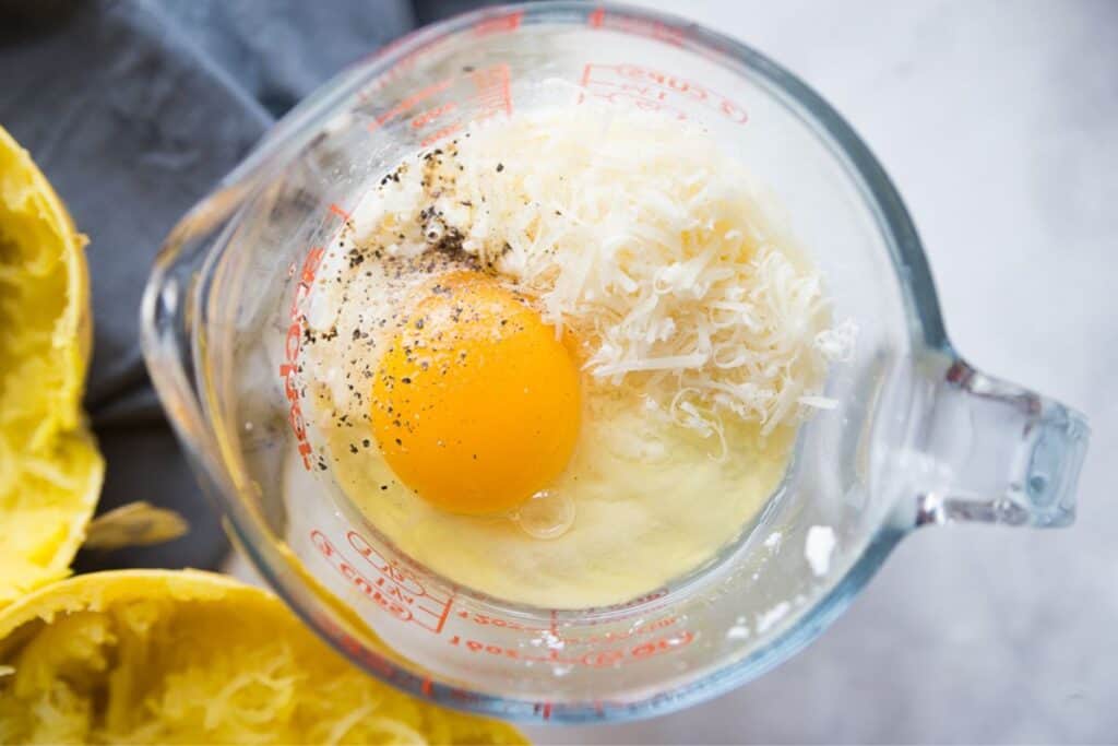 Egg, ricotta, parmesan cheese, and pepper in a glass measuring cup.