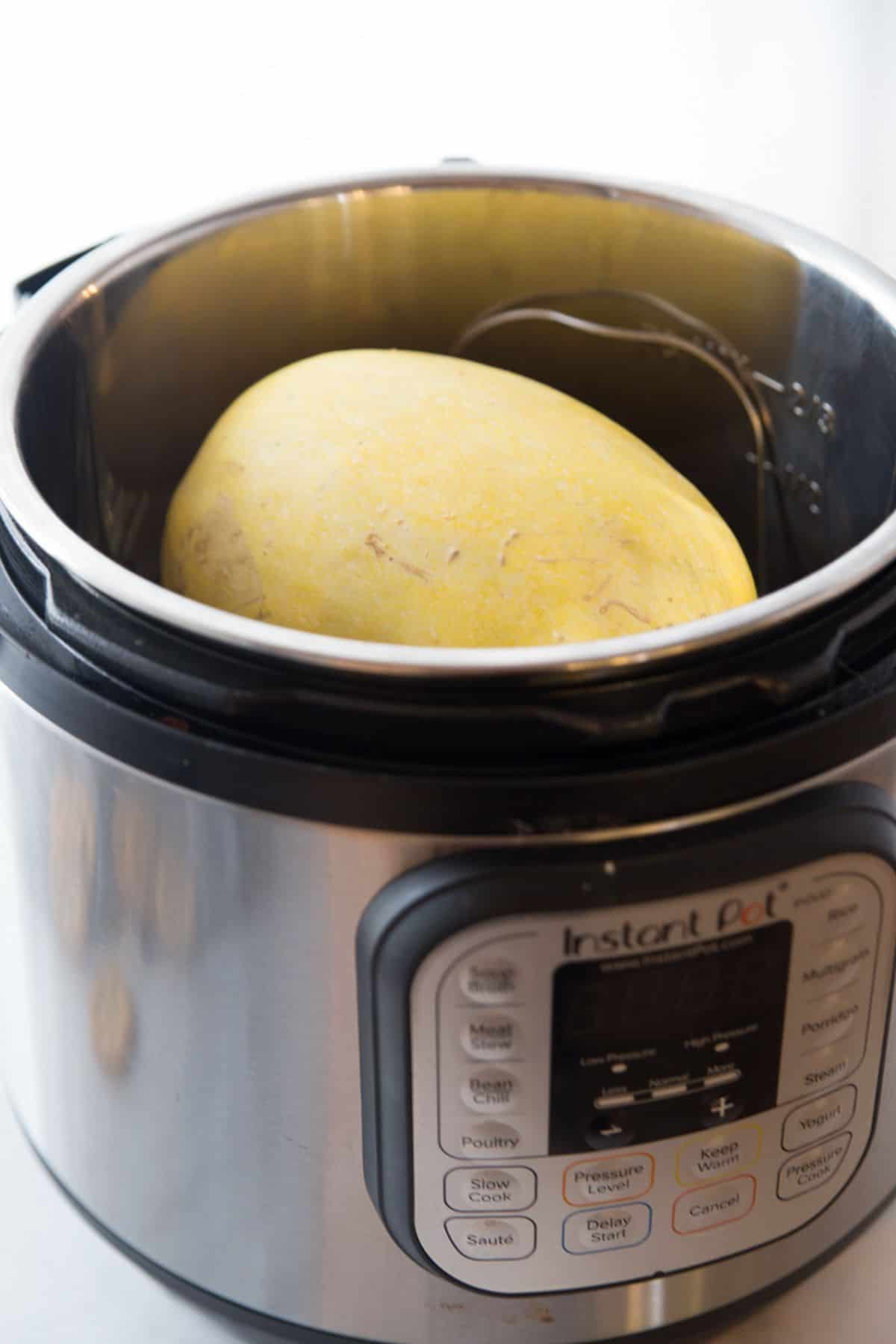 An instant pot with a whole, uncooked spaghetti squash.