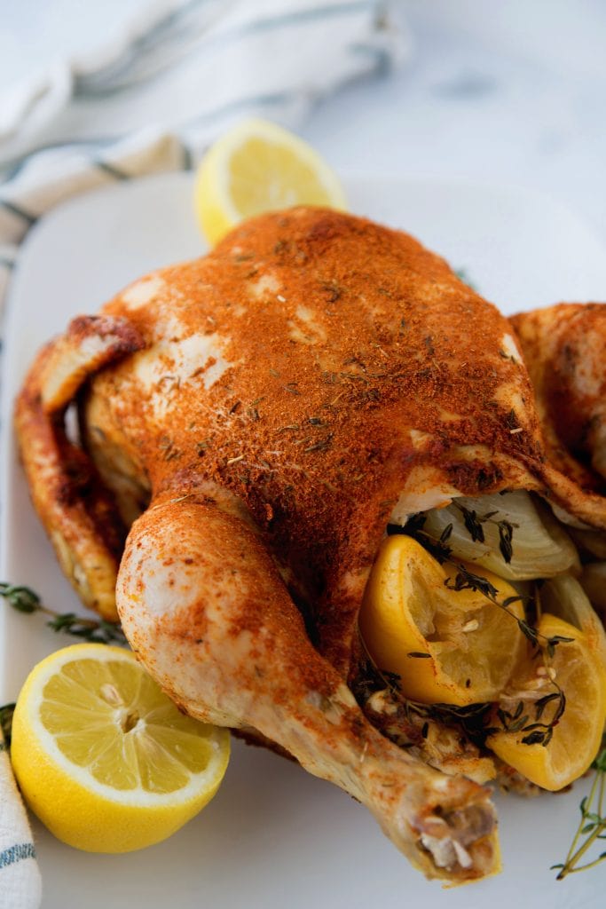 A cooked Whole Chicken made in the Instant Pot sitting on a white plate next to cut lemons and fresh thyme 