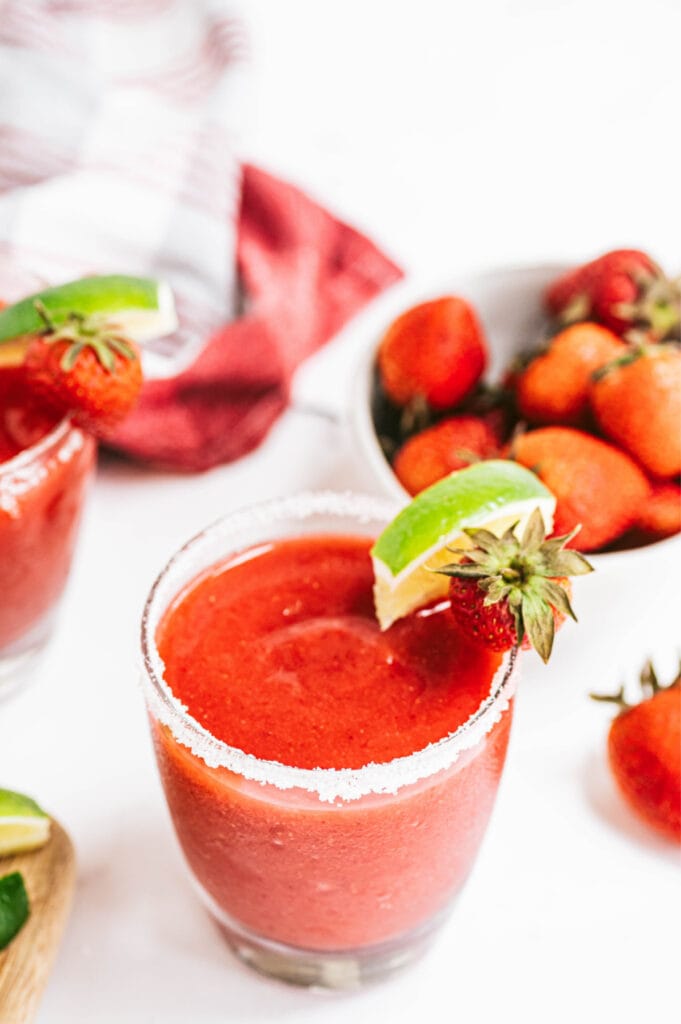 An overhead shot of a salt rimmed glass filled with Frozen Strawberry Rhubarb Margarita garnished with lime and strawberries