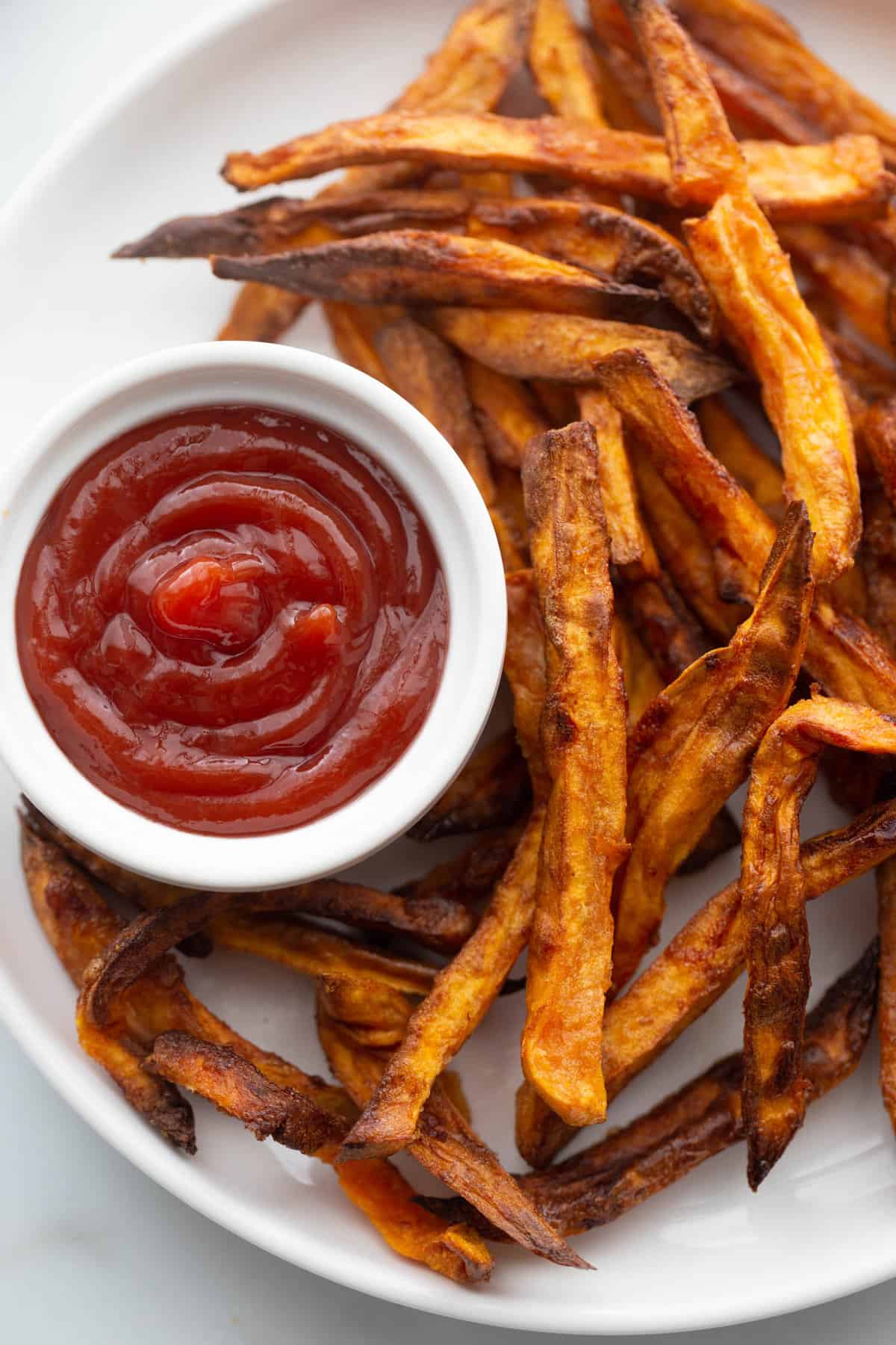 Homemade sweet potato fries on a white plate with a side of ketchup.