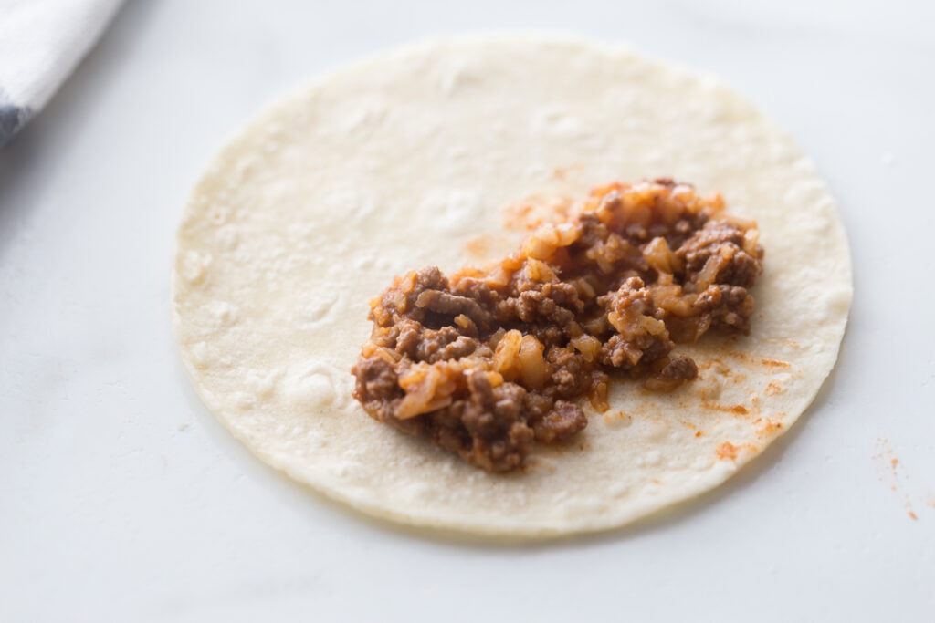 A corn tortilla filled with cauliflower beef taquito filling on a white counter top