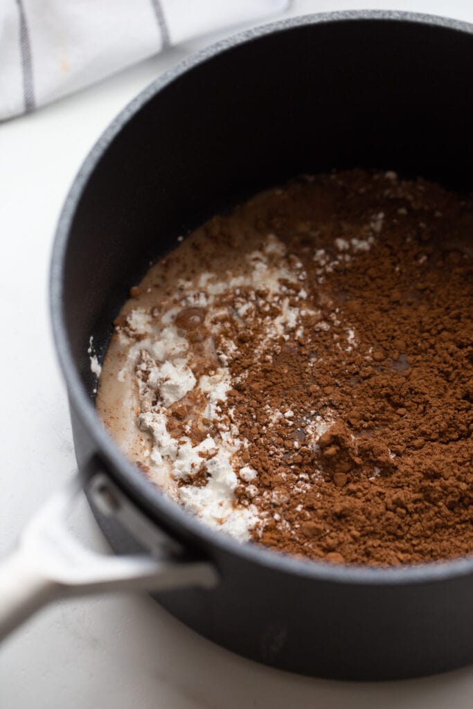 Cocoa powder, cornstarch, and milk in a saucepan for vegan chocolate pudding
