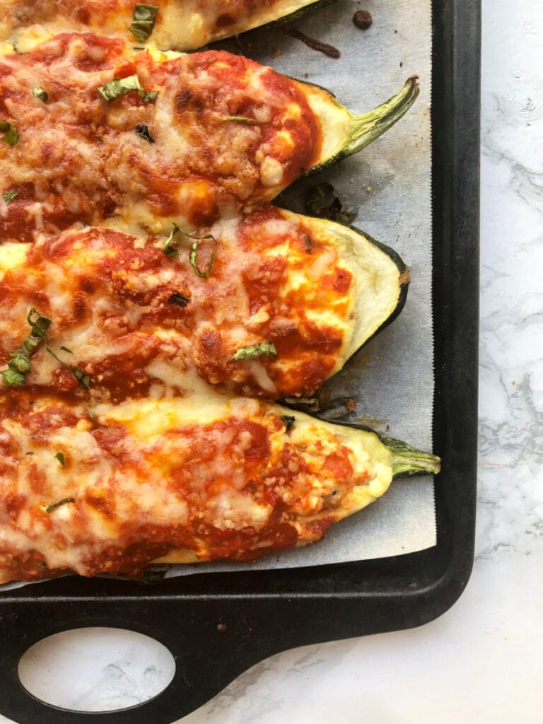 Baking sheet with Lasagna Stuffed Zucchini Boats on a marble backdrop. Boats have been broiled and the cheese is bubbly and crispy.