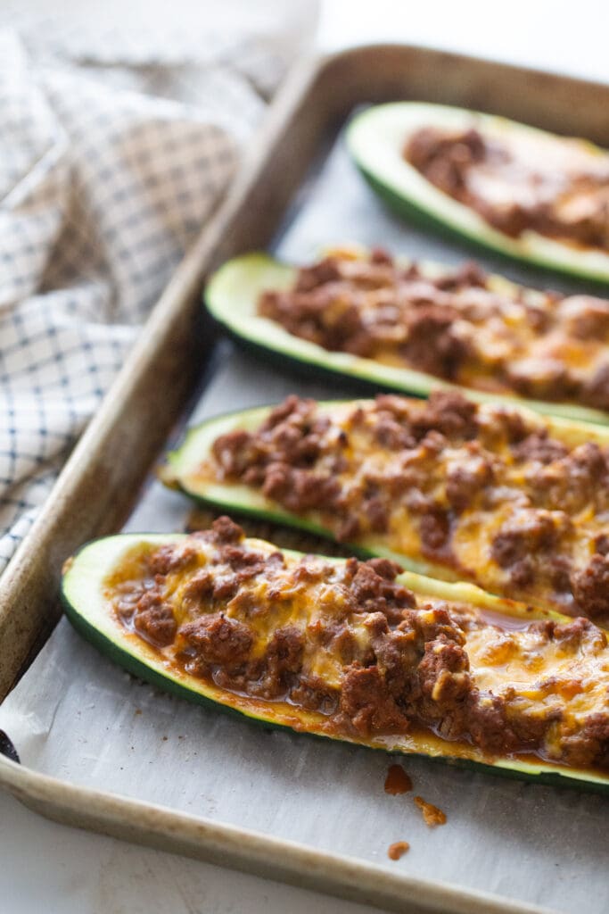 Parchment lined baking sheet with four zucchini taco boats topped with ground beef and cheese.