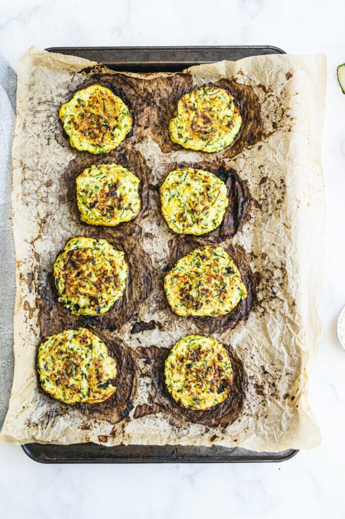 Overhead image: Baked zucchini fritters on a parchment lined sheet pan 