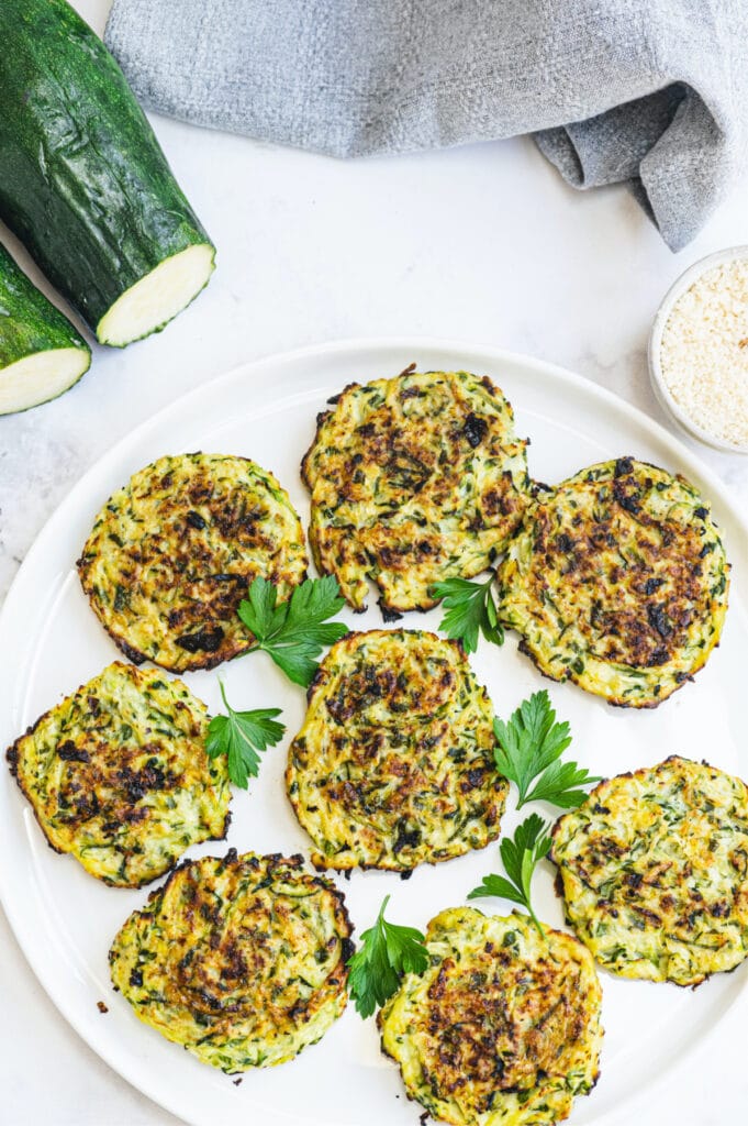 Overhead photo of zucchini fritters on a white plate with zucchini halves on the side.