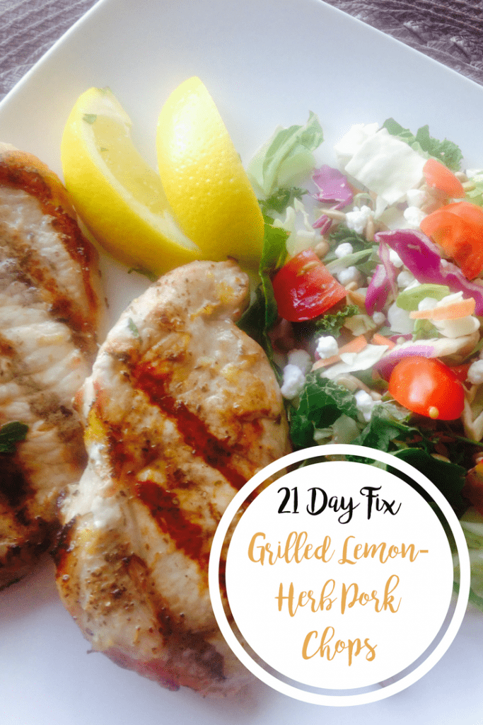 Two Grilled Lemon-Herb Pork Chops next to a side salad and lemon wedges on a square white plate with the text overlay- 21 Day Fix Grilled Lemon-Herb Pork Chops