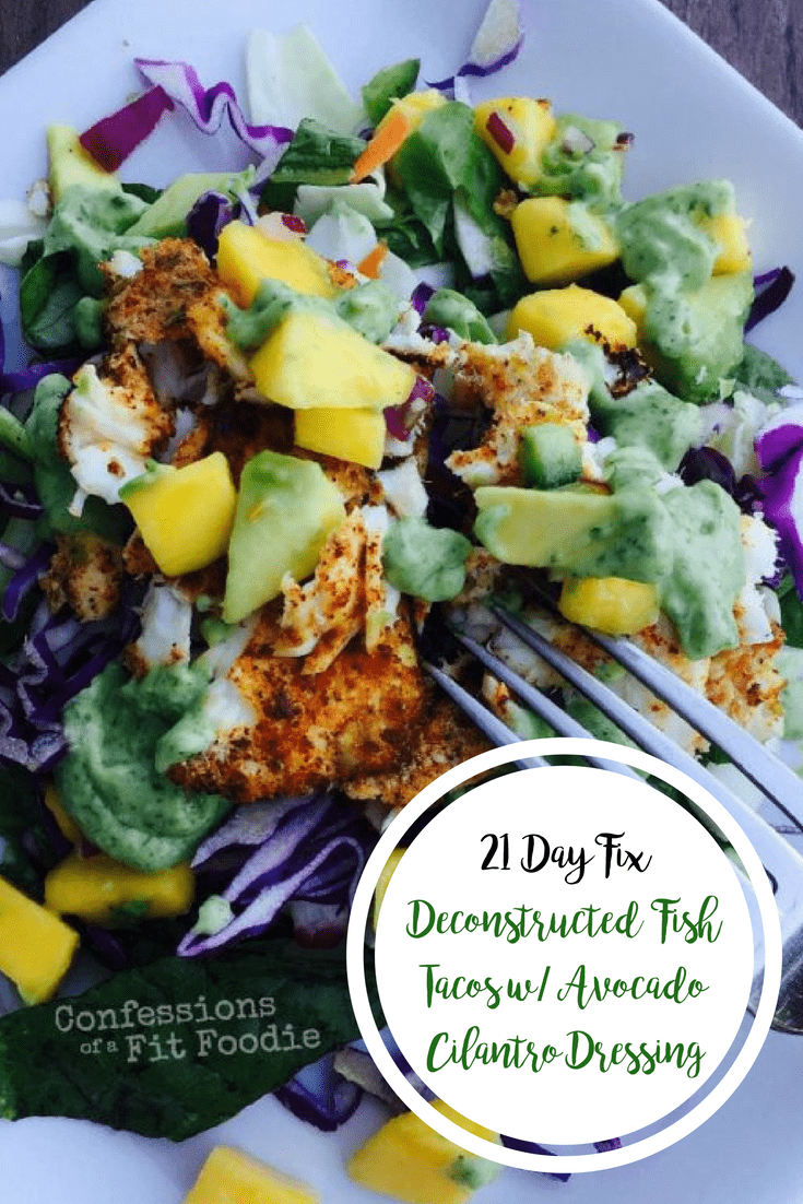 Fish taco salad with red cabbage, diced mango, diced avocado, taco seasoned fish, and greens on a square white plate and a fork poised for eating and the text overlay- 21 Day Fix Deconstructed Fish Tacos w/ Avocado Cilantro Dressing