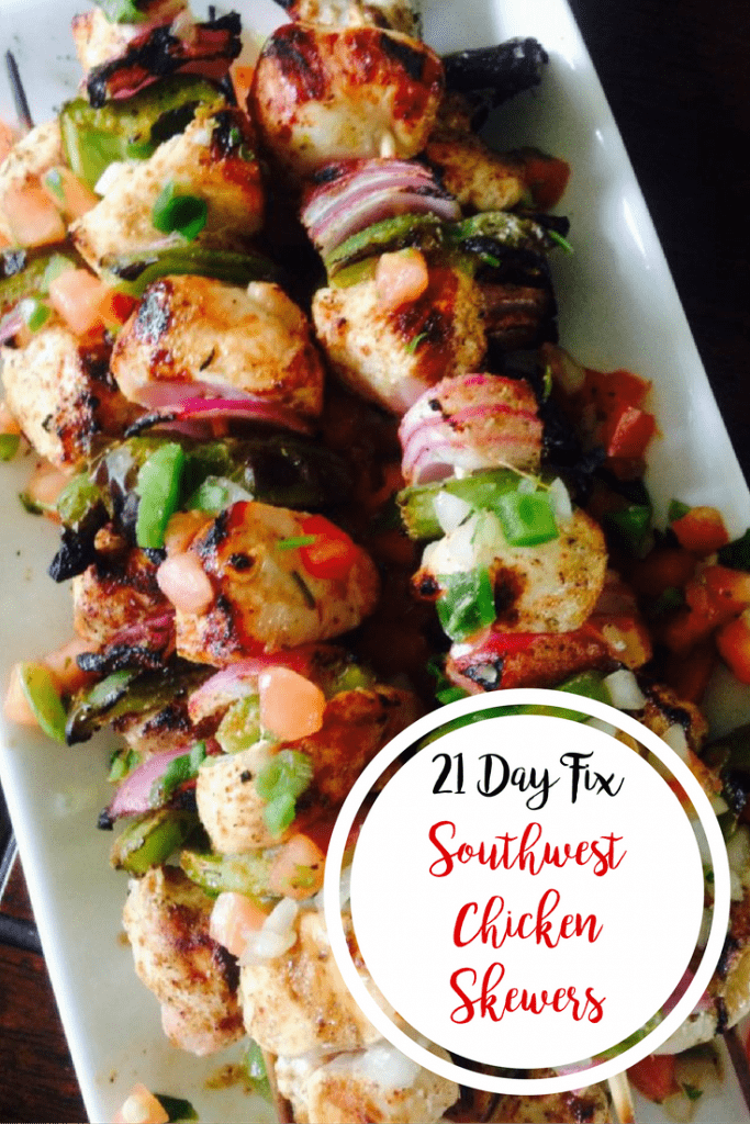 Grilled southwest chicken, green pepper, and red onion alternate on wooden skewers. Many are piled on a long rectangular plate with a dark background and text overlay- 21 Day Fix Southwest Chicken Skewers